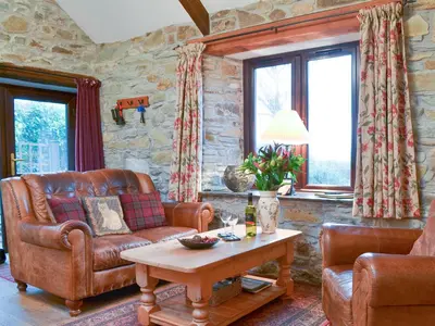 a living room with a leather couch and a table at Campion Cottage in Saint Teath