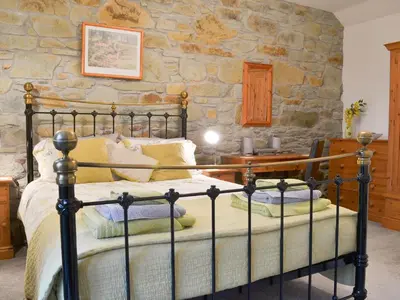 a bedroom with a bed and a stone wall at Campion Cottage in Saint Teath