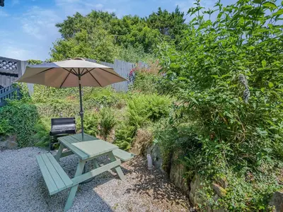 a picnic table with an umbrella and a chair at Home Park Farm Cottages B in Lanteglos