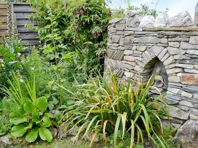 a stone wall in a garden with plants at Well Barn in Lanteglos