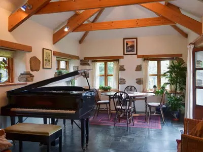 a living room with a piano and a table at Well Barn in Lanteglos