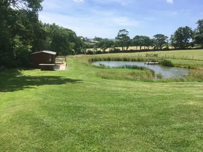 a park with a pond and a bench in the grass at The Stable in North Petherwin