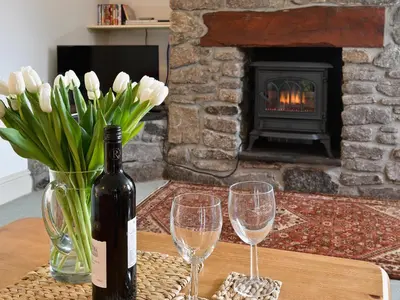 a bottle of wine and two glasses on a table with a fireplace at Stable End in Trewen