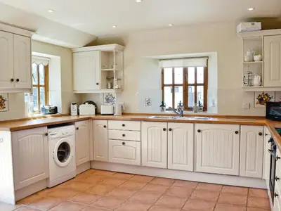 a kitchen with white cabinets and a washer and dryer at Barfield's Cherry Tree Cottage in Warbstow