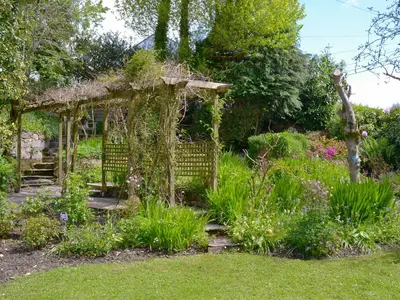 an old pergola in a garden with flowers at The Thatch Cottage in South Petherwin