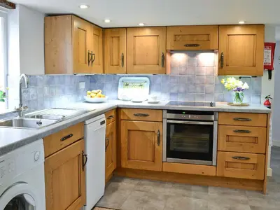 a kitchen with wooden cabinets and a sink and a dishwasher at The Thatch Cottage in South Petherwin