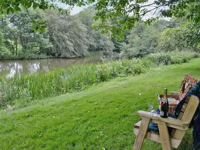 a picnic table with wine glasses on it next to a river at The Granary in Egloskerry