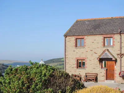 a brick house with a wooden door and a bench at Porth View in Saint Mawgan