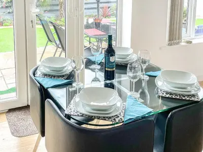 a glass table with plates and glasses and a bottle of wine at Palm Villa in Saint Columb Minor