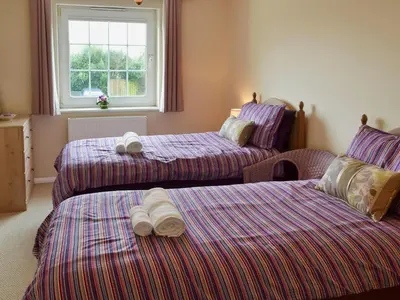 two beds in a room with purple sheets and a window at The Old Butchers in Crantock