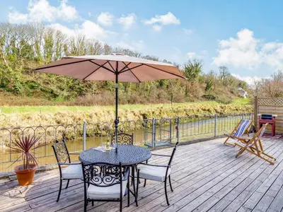 a table and chairs with an umbrella on a deck at Creekside in Little Petherick