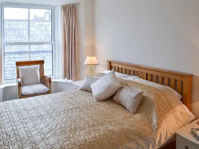 a bedroom with a bed and a chair and a window at Sandpipers in Padstow