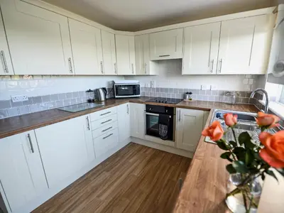 a kitchen with white cabinets and a vase of orange roses at The Yellow House in Padstow