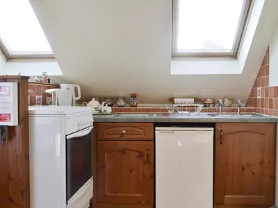 a kitchen with wooden cabinets and a white dishwasher at Spring Tides in Padstow
