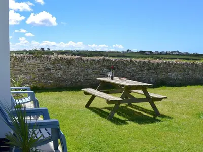 a picnic table in the grass with a drink on it at St Cadoc Cottage in St Merryn