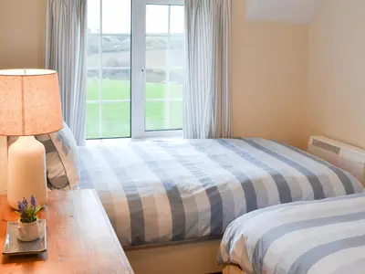 a bedroom with two beds and a window at St Cadoc Cottage in St Merryn