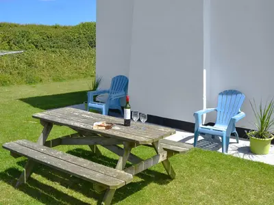 a picnic table with two blue chairs and a bottle of wine at St Cadoc Cottage in St Merryn