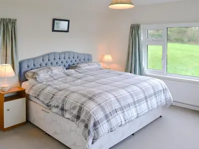 a bedroom with a bed with a plaid blanket and a window at Tregunna Cottage in Wadebridge