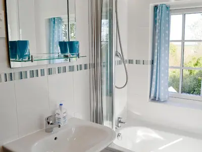 a white bathroom with a sink and a shower at Tregunna Cottage in Wadebridge