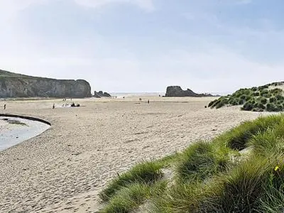 a sandy beach with people in the water and cliffs at Blue Waves in Perranporth