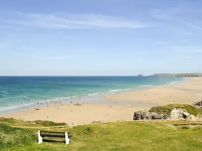 a bench on a hill overlooking a beach with people at Blue Waves in Perranporth