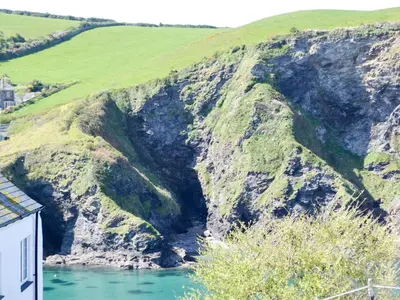 a cave in the side of a mountain next to a river at Cobblers Cottage in Port Isaac
