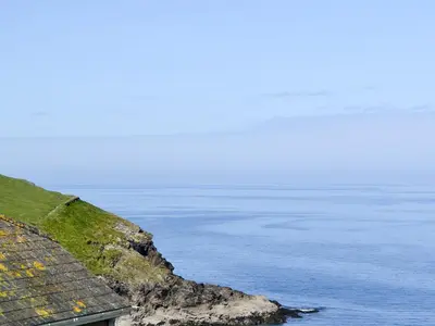 a building on the side of a cliff next to the ocean at Cobblers Cottage in Port Isaac