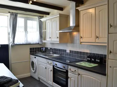 a kitchen with white cabinets and a washer and sink at Cobblers Cottage in Port Isaac