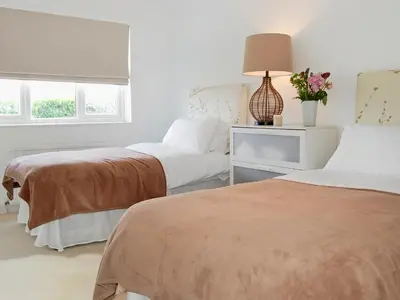 two beds in a white room with a lamp and flowers at The Lookout in Port Isaac