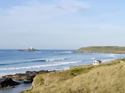 a small white house on a hill next to the ocean at Ash Tree Cottage in Carnbrea