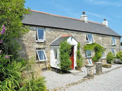 a stone house with a red door on a gravel road at The Farm House in Porkellis