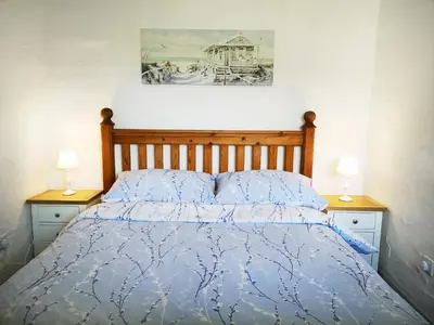 a bed with a blue comforter and two night stands at Maple Barn in Porthtowan