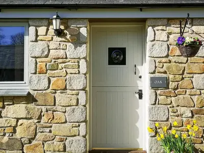 a stone house with a white door and a stone wall at Oak Barn in Porthtowan