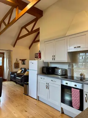 a kitchen with white cabinets and a living room at Rose Cottage, Tregolls Farm in Saint Wenn