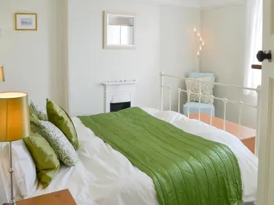 a white bedroom with a green blanket on a bed at Tregatta Terrace in Tintagel