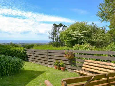 a wooden bench sitting next to a fence with plants at Kilcummer Stables in Tintagel