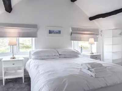 a white bedroom with a bed with white sheets and two lamps at Pollards Cottage in Forrabury
