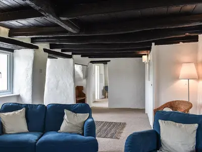 a living room with a blue couch and wooden ceilings at Pollards Cottage in Forrabury