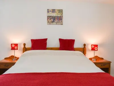 a bedroom with a bed with red pillows and two lamps at Dove Cottage in Lezant
