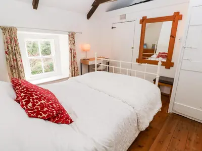 a bedroom with a white bed with red pillows and a mirror at Honeysuckle Cottage in St. Agnes