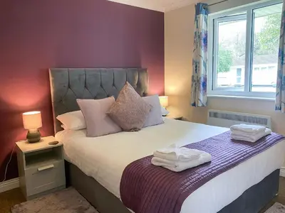 a bedroom with a bed with purple walls and a window at Talland Bay in Saint Cleer