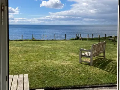 a bench sitting on the grass near the ocean at 3 The Coastguards in Downderry