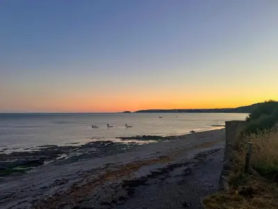 a beach with people in the water at sunset at Coastguard Cottage in Downderry