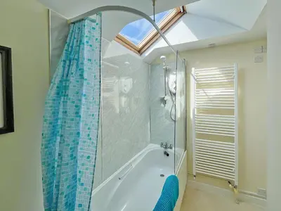 a bathroom with a tub and a shower with a window at Coastguard Cottage in Downderry