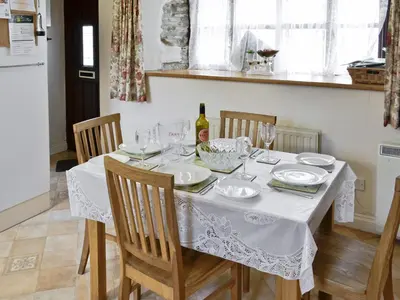 a dining room table with a white table cloth and a bottle of wine at Florin Cottage in Lerryn