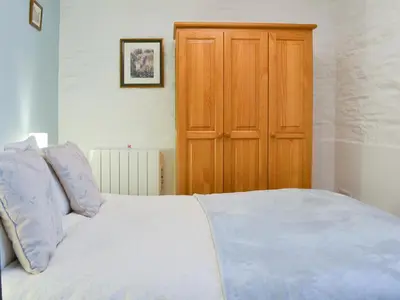 a bedroom with a white bed and a wooden cabinet at Trenay Barns Cottage in Warleggan