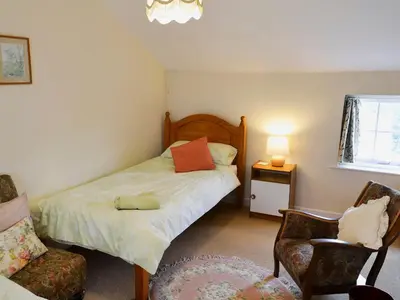 a small bedroom with a bed and a chair at Watercolour Cottage in Lerryn