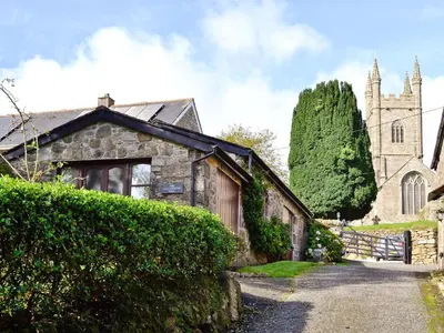 an old stone house with a church in the background at The Blacksmiths Shop in Lanlivery