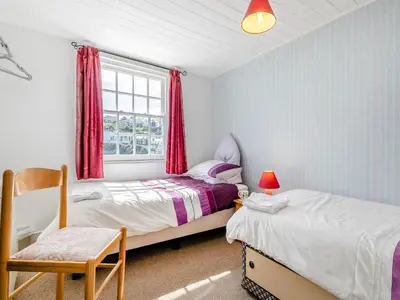 a bedroom with two beds and a chair and a window at Memory Cottage in Mevagissey