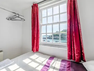 a bedroom with red curtains and a window at Memory Cottage in Mevagissey